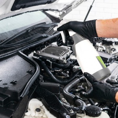 Pessoa com luvas pretas a aplicar borrifador no motor aberto de carro branco