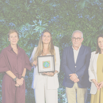 Grupo de quatro pessoas em roupa formal com fundo verde de plantas, uma pessoa segura um quadro com desenho do globo terrestre.