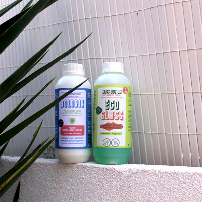 Dois frascos brancos e verde para produtos, com rótulos distintos, sobre parede branca perto de plantas