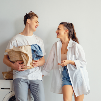 Casal jovem sorridente com roupa casual junto a máquina de lavar roupa