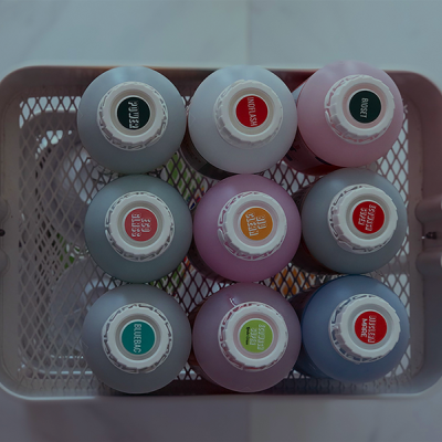 Nove garrafas coloridas organizadas em cesto de plástico cinza vistas de cima