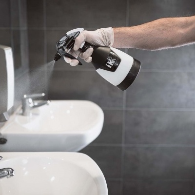 Homem a pulverizar líquido num lavatório branco com torneira cromada numa casa de banho