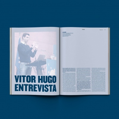 Revista aberta com entrevista de Vitor Hugo e fotografia de homem a falar no microfone