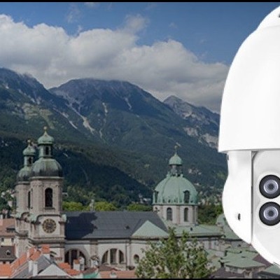 Câmara de segurança branca montada na parede com vista de cidade e montanhas ao fundo