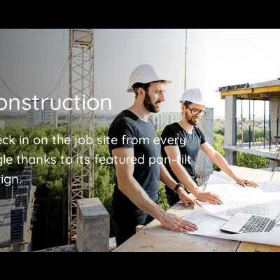 Dois homens com capacetes a ver plantas num local de construção com grua e laptop