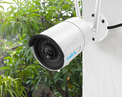 Câmara de segurança branca Reolink com gotas de água instalada numa parede branca, fundo com plantas verdes