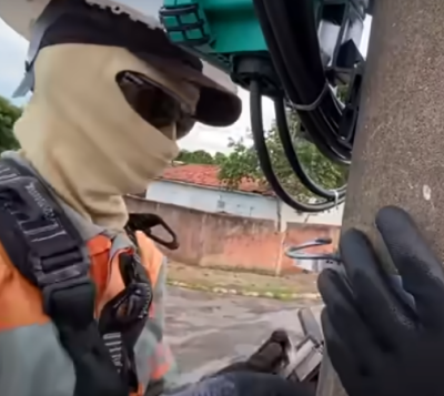 Trabalhador com roupa de proteção manipula poste com cabos elétricos