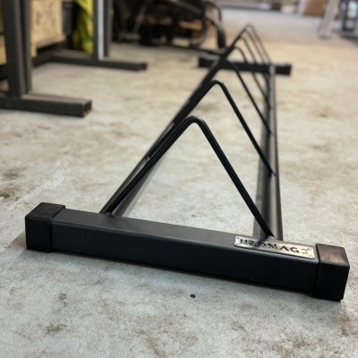 Suporte metálico preto para bicicletas com estrutura triangular e etiqueta 'IRMAG'