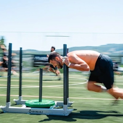 Homem a empurrar trenó de treino com pesos verdes numa pista de treino ao ar livre