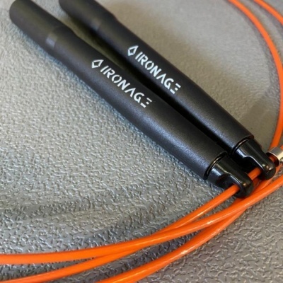 Corda de saltar preta e laranja com marca IRONAG sobre superfície cinzenta