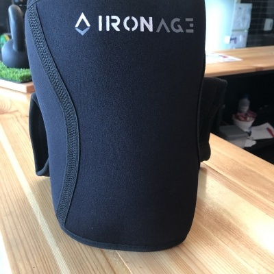 Cinta suporte para joelho preta com logo IRONAGE sobre mesa de madeira