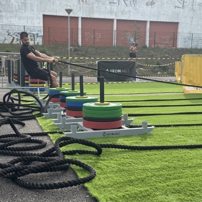 Aparelhagem de treino com placas coloridas e cordas de puxar em campo verde e homens a correr ao fundo