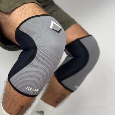 Joelheiras cinza e pretas com texto IRON numa perna de homem