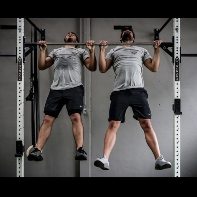 Dois homens a fazer tração numa barra fixa branca com texto IRON AG em ginásio.