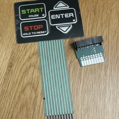 Placa eletrónica com botões START, STOP, ENTER e fita flexível sobre mesa de madeira.