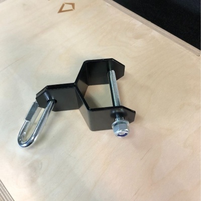 Suporte metálico preto com parafuso e argola sobre superfície de madeira clara