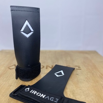 Protetores de pulso pretos com logótipo IRONAGE sobre superfície de madeira.