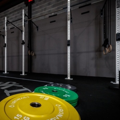 Placas de peso amarelas, verdes e pretas numa academia com estrutura metálica branca e argolas de ginástica