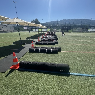 Campo desportivo com sacos de peso pretos IRON ACE alinhados e cones de trânsito laranja