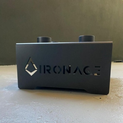 Base metálica preta fosca com recorte da palavra IRONAGE e logótipo, sobre chão cinzento