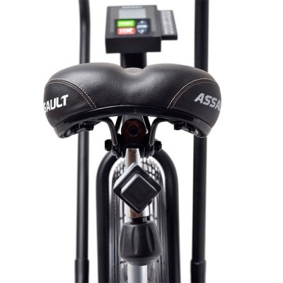 Banco preto perfurado de bicicleta ergométrica com texto ASSAULT e painel digital ao fundo