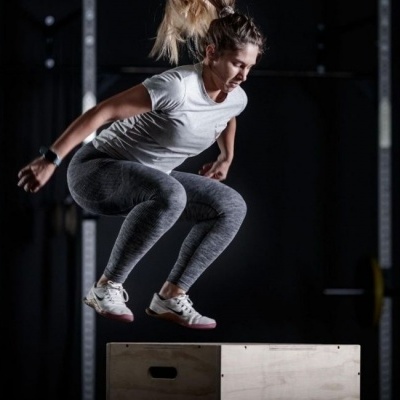 Mulher a fazer salto num banco de madeira num ginásio escuro