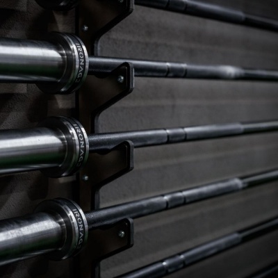 Barras olímpicas de peso de aço em suportes pretos na parede cinza