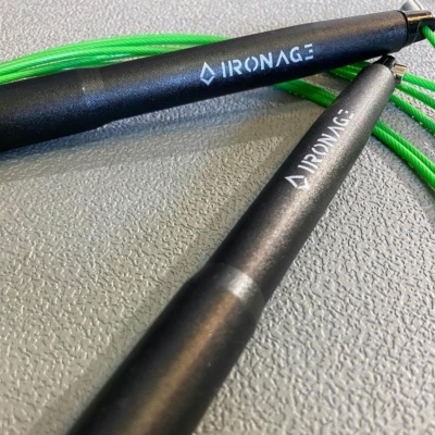 Corda de saltar preta com corda verde sobre fundo cinza texturizado.