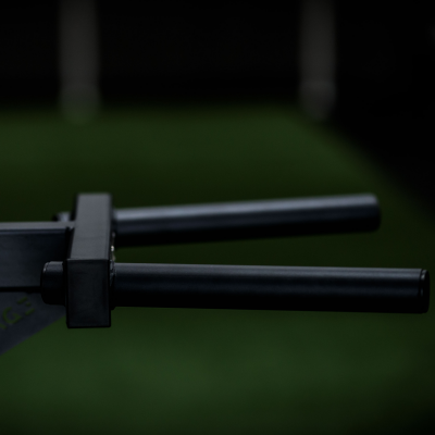 Objeto metálico preto com dois braços cilíndricos paralelos sobre fundo verde desfocado