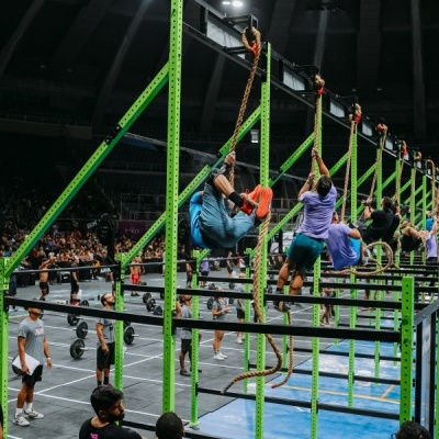 Estrutura metálica verde para treino em ginásio desportivo com pessoas a escalar.
