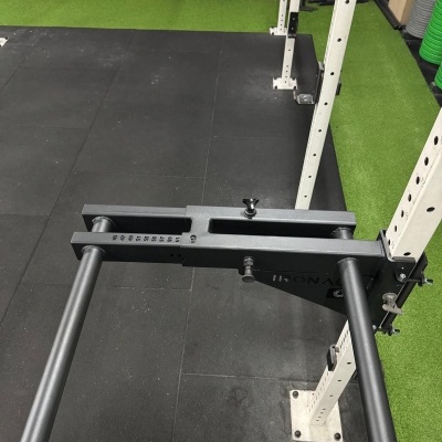 Suporte de barra de ferro preta ajustável numa estrutura branca com chão preto e relva verde ao fundo