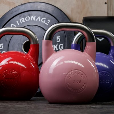 Três kettlebells coloridos à frente de discos de peso com texto 'IRONAGE' e '5 KG'