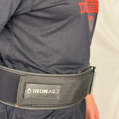 Cinto de suporte lombar preto com etiqueta 'IRONAGE', usado numa pessoa com camiseta preta e estampado vermelho.