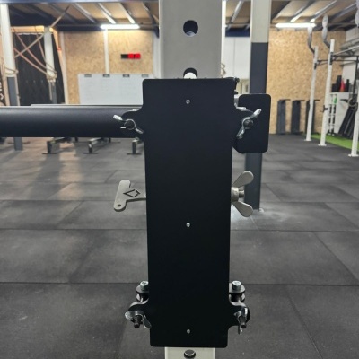 Aparelho de musculação preto fixado em estrutura branca num ginásio