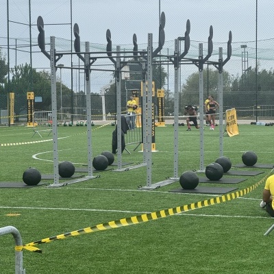 Estrutura metálica cinzenta para exercícios de CrossFit com bolas medicinais pretas em campo de relva sintética