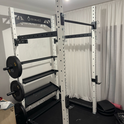 Estrutura de treino de musculação em metal branco e preto com discos de peso e barra de puxar em sala com cortinas brancas