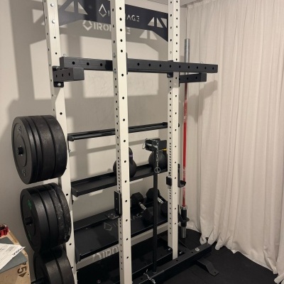 Estrutura metálica para treino de força com pesos e prateleiras junto a uma cortina branca.