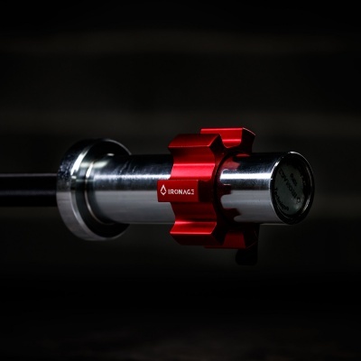 Barra de levantamento de peso de metal prateado com peça vermelha em fundo escuro