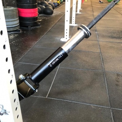 Braço de ancoragem para barra de exercício preto e prateado fixado em estrutura branca numa academia