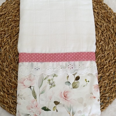 Toalha branca com barra rosa e estampado floral colocada sobre base de ráfia