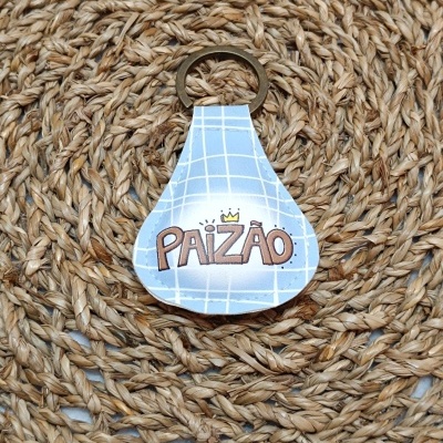 Porta-chaves azul claro com grelha branca e texto PAIZÃO sobre tapete de fibras naturais.