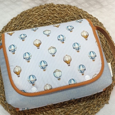 Mala dobrável com padrão de balões de ar quente e bordas castanhas sobre base de fibra natural trançada