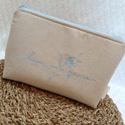 Bolsa bege com fecho azul claro e bordado azul claro com texto e flor