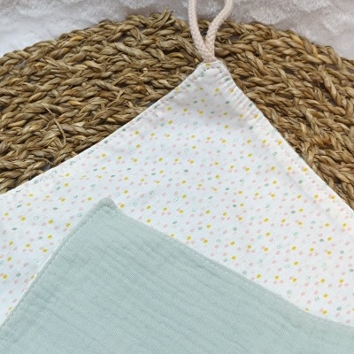 Dois panos de cozinha sobre suporte redondo de fibra natural, um branco com pontos coloridos e outro azul esverdeado liso