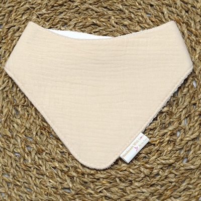 Babete bege claro com etiqueta colocada sobre tapete de palha trançada