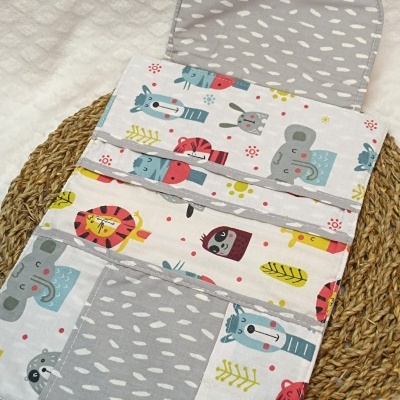 Produto tecido colorido com animais e padrão cinza, colocado sobre base de palha e tecido branco texturado