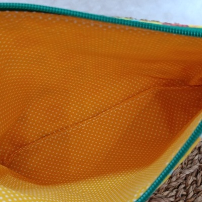 Interior de bolsa amarela com bolinhas brancas e zíper verde sobre superfície trançada castanha