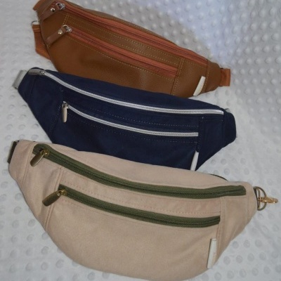 Três bolsas de cintura castanha, azul escuro e bege sobre superfície branca texturada