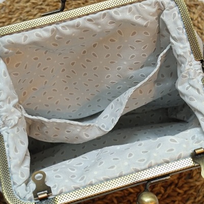 Interior de mala pequena com fecho metálico dourado e revestimento cinzento com padrão de folhas brancas