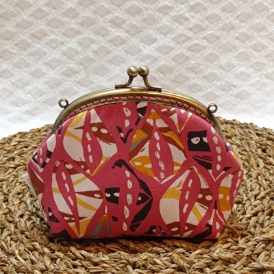 Carteira pequena com fecho de metal dourado e padrão colorido sobre superfície de ráfia